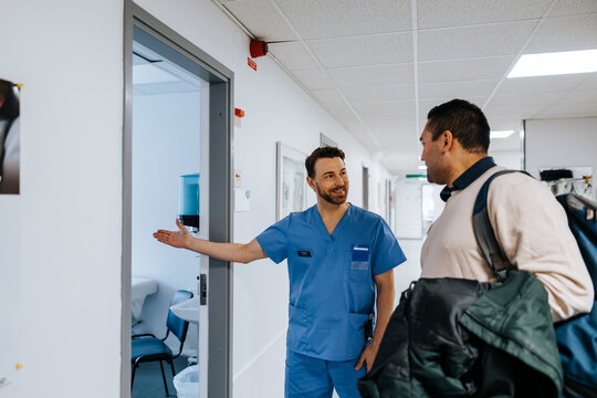 Smiling mature male doctor escorting patient through doorway of examination room at hospital