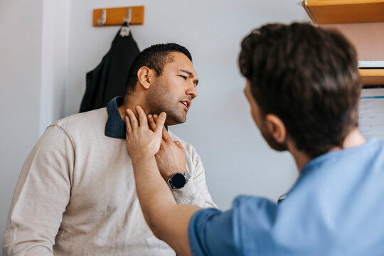 Male medical expert checking neck problem of patient in examination room