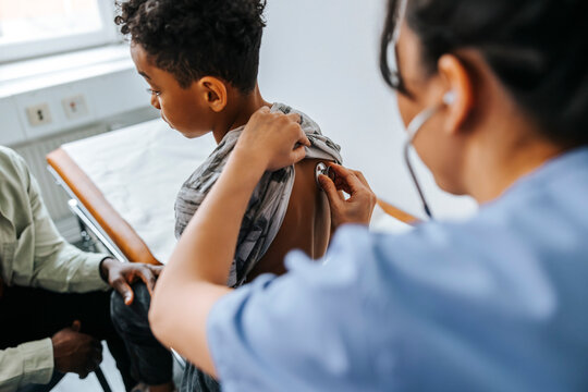 Female pediatrician examining boy's back with stethoscope in examination room