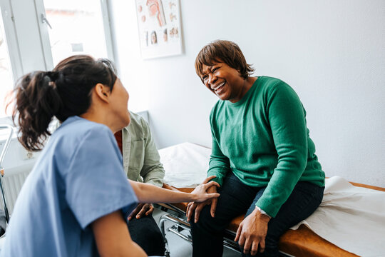 Happy senior woman sitting on examination table during visit with female doctor at hospital