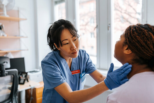 Female medical expert checking lymph nodes of young patient in examination room at hospital