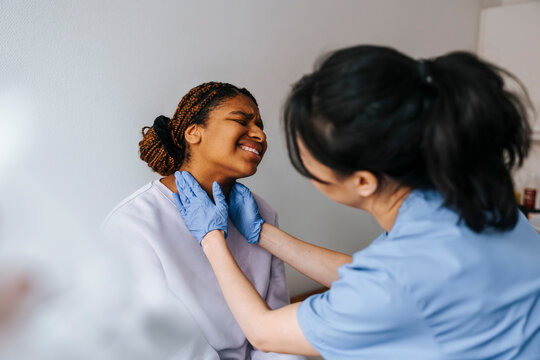 Female medical professional checking lymph nodes of anxious patient in examination room at hospital