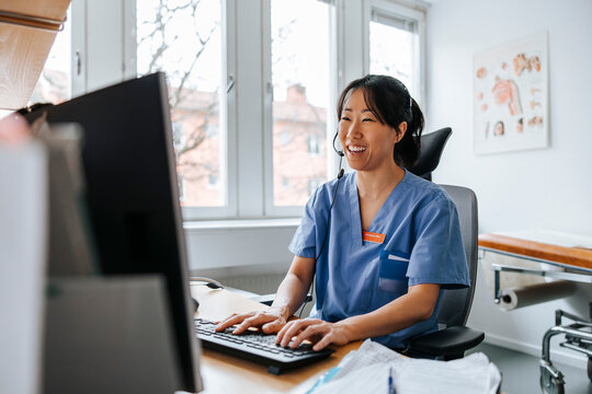Happy female medical expert wearing headset and doing online consultation on video call through computer at clinic