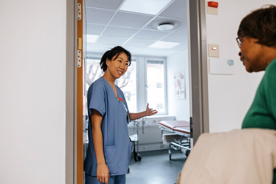Smiling female doctor escorting senior patient through doorway of examination room at hospital