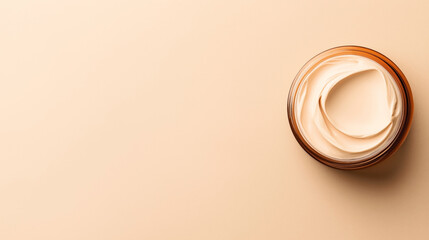 Overhead view of an open jar with beige face cream on a matching light brown background for minimalist skincare or beauty product concept