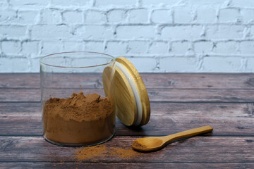 Glass jar of cocoa powder with a wooden lid and spoon on a rustic table.