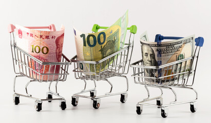 100 US dollar, 100 Chinese yuan and 100 euro bills in a miniature supermarket shopping cart