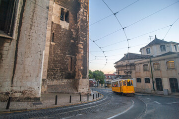 A charming yellow tram navigates the winding streets of Lisbon, Portugal, as the sun sets, highlighting the historic architecture surrounding the route