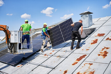 Workers building solar panel system on metal rooftop of house with assistance of crane lift. Two...