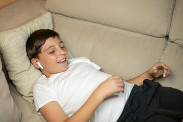 Happy child listening to music on headphones relaxing on the sofa at home