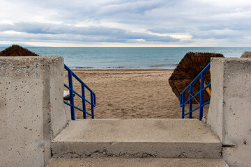 Entrance to an empty off-season sandy beach with beach umbrellas on the ground under stormy skies at Pomorie, Province of Burgas, Bulgarian Black Sea coast