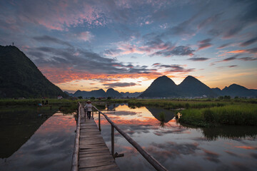 A middle-aged woman was riding her bicycle across a wooden bridge in Bac Son Village. Beautiful sunset in the evening