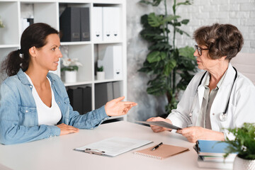 Female middle-aged patient complaining about illness diseases symptoms to elderly senior doctor general practitioner gynecologist in hospital