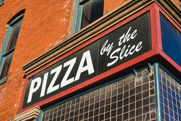 Fototapeta premium Unique Pizza by the slice sign above a pizza shop