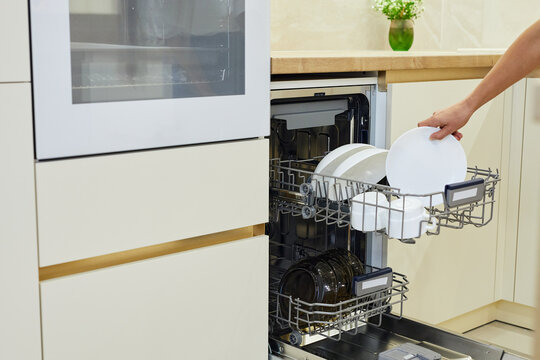 Woman loading plates into an open dishwasher in a modern kitchen, carrying out daily domestic tasks