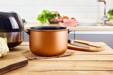 Domestic electric multi cooker on wooden table. Housewife using multi-cooker in kitchen. Space for...
