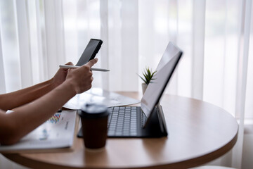 Fototapeta premium Businesswoman using smartphone and analyzing charts on tablet at home office