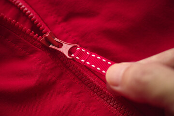 A man unzipping his red jacket. Close up.