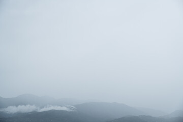 Fog-shrouded mountain range with blue hues and cumulus clouds – moody landscape with layered peaks and a serene, atmospheric tone