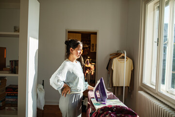 Woman standing by ironing board looking frustrated during household chores