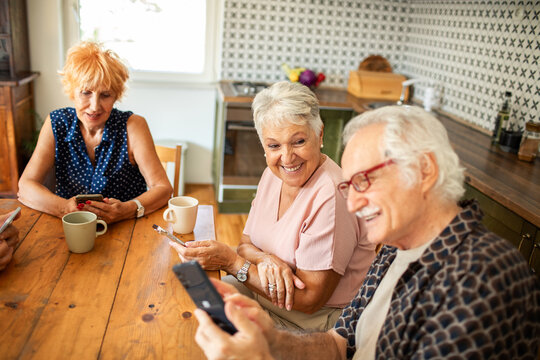 Group of senior friends laughing together while looking at smartphone in kitchen