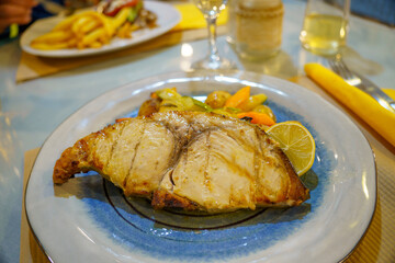 Mediterranean cuisine: swordfish fillet with mixed vegetables and lemon on a blue and white plate. Close-up