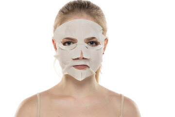 Beautiful young woman posing with a facial white paper mask on her face. Skin care and treatment, spa, natural beauty and cosmetoogy concept.