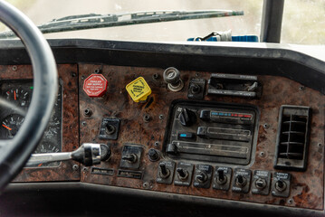 Interior View of an Old Semi Truck Dashboard: Dusty Controls for Air Brakes, Cruise Control, and Climate Control with a Classic Wood Grain Finish, Featuring Keys in the Ignition, switches and sliders
