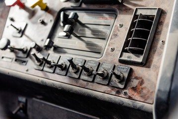 Interior View of an Old Semi Truck Dashboard: Dusty Controls for Air Brakes, Cruise Control, and Climate Control with a Classic Wood Grain Finish, Featuring Keys in the Ignition, switches and sliders