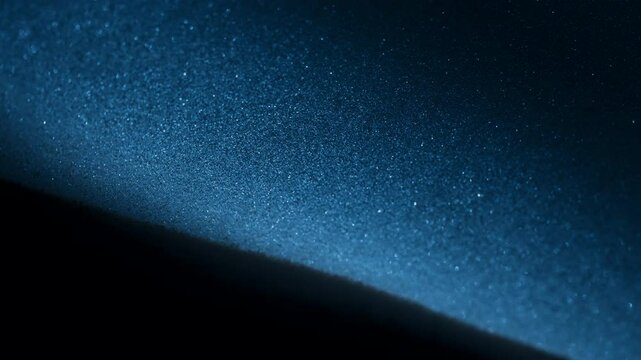 Blue light shining on dust particles falling in slow motion. Abstract macro shot. 