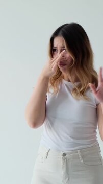 Discontent Caucasian woman upset by bad or nasty smell, standing on white background. Concept of a displeasure and shock. Vertical video.