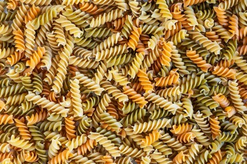Three Colors Rotini Pasta. Pasta fusilli tricolor background. Abstract texture of healthy pasta. Pattern of macaroni. Pastel multicolor food backdrop. Uncooked colored noodles.