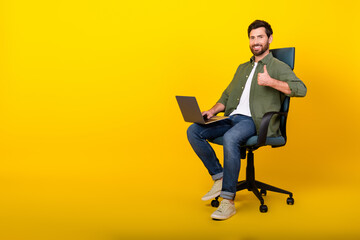 Full length portrait of nice young man sit chair netbook thumb up wear shirt isolated on yellow...