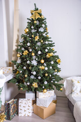 Christmas tree is decorated with gold and silver toys and gifts in a white classic interior. Christmas tree at home. Christmas tree decoration.