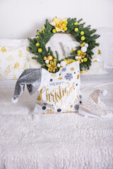 Christma spillow with gold lettering on a white bedspread with a festive wreath in the background