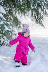 Little girl in pink winter clothes walks through a snowy park. A snowy winter day in the park. Winter activities.