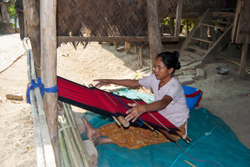 South asian tribal woman working on a handloom machine sitting inside her home