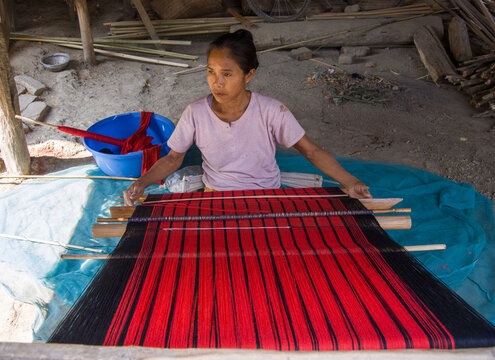 South asian tribal woman working on a handloom machine sitting inside her home