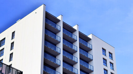 Modern high-rise apartment building  in white, stand tall against a blue sky, exemplifying innovative urban architecture with sleek, angular designs. © Grand Warszawski
