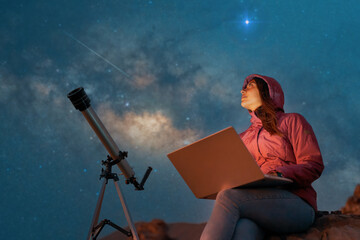 portrait woman sitting in the desert with a laptop next to a telescope at night watching the starry sky, astronomy and stargazing concept  © freechoice