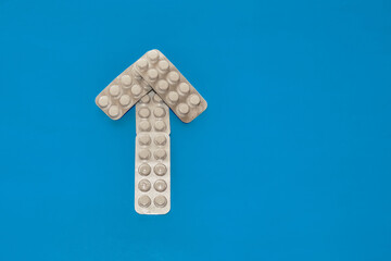 An arrow made of blister packs of white tablets pointing upwards against a blue background, close-up, successful treatment, recovery from illness, path to healing.