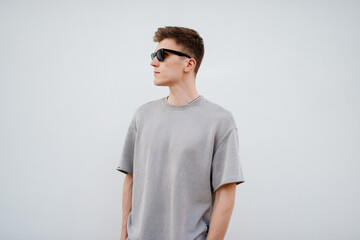 A Stylish Young Man Wearing Sunglasses Poses Against a Clean, Minimalist Background