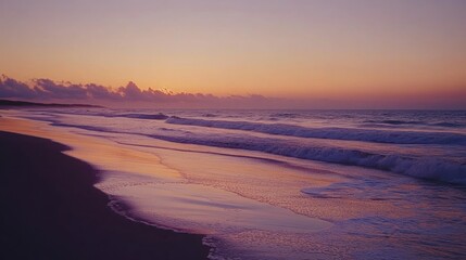 A serene sunset over the ocean with waves crashing on the sandy shore.