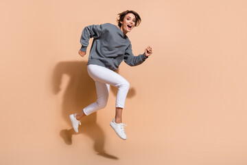 Full length photo of positive girl wear pullover white trousers jumping run shopping to empty space isolated on beige color background