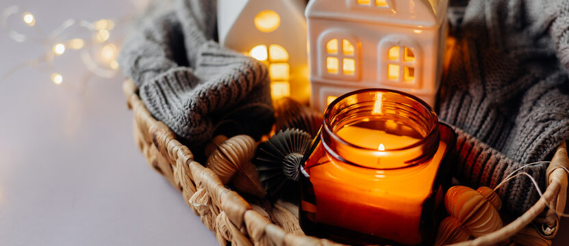 Winter or autumn cozy interior decorations. Burning candle, ceramic houses, cozy sweater. Christmas cozy winter home decor. Long Banner for design, website