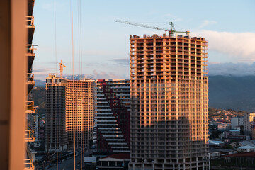 Tall buildings rising under construction, bathed in golden sunset light with crane silhouettes and geometric lines