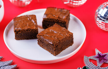 Dark chocolate brownie cakes in a plate on a red background for Christmas holidays