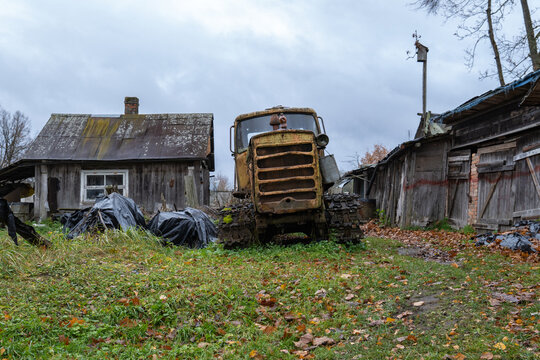Old agricultural crawler tractor DT-75. Manufactured during Soviet times. The backyard of an old half-collapsed house.