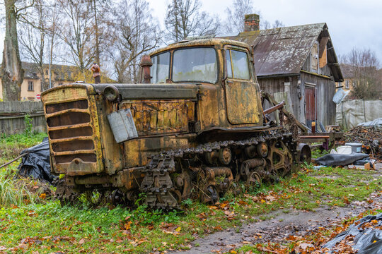 Old agricultural crawler tractor DT-75. Manufactured during Soviet times. The backyard of an old half-collapsed house.