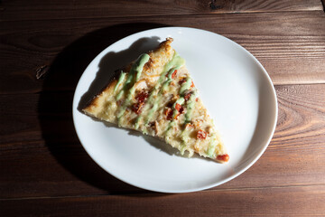 close-up of one piece of pizza on a white plate. Wooden table, top view, hard shadow